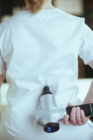 Healthcare time. Closeup on female medical massage therapist in spa salon with massage pistol.の写真素材