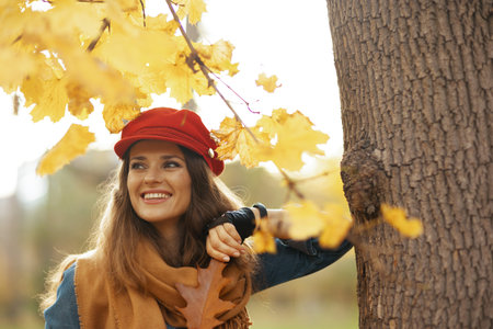 Hello autumn. happy stylish 40 years old woman in jeans shirt and red hat with autumn leaf and scarf...