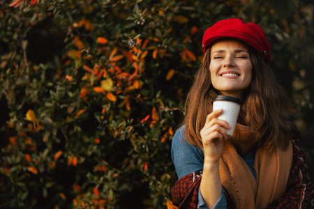 Hello autumn. smiling young woman in red hat with autumn leaves, scarf and coffee in the city park.