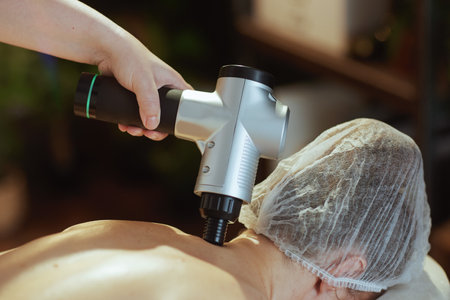 Healthcare time. Closeup on medical massage therapist in spa salon with massage pistol massaging clients neck.の写真素材