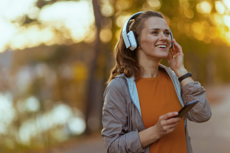 Hello autumn. smiling elegant female in fitness clothes in the park with headphones.