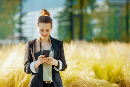 pensive modern middle aged business woman in business district in black jacket using smartphone.の写真素材