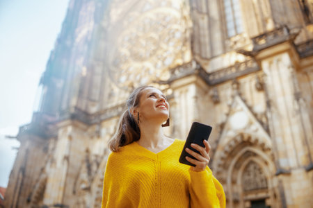 happy trendy traveler woman in yellow blouse in Prague Czech Republic having excursion, using smartphone and walking.の写真素材