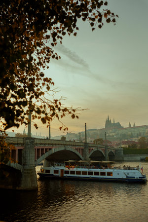 landscape with Vltava river, St. Vitus Cathedral and boat at sunset shot through the foliage in autumn in Prague, Czech Republic.の写真素材