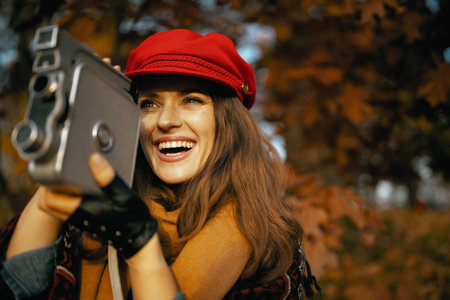 Hello autumn. happy stylish 40 years old woman in red hat with retro video camera, scarf and gloves...