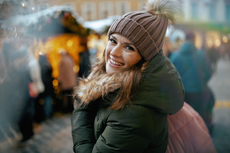 smiling modern female in green coat and brown hat at the Christmas fair in the city.の写真素材
