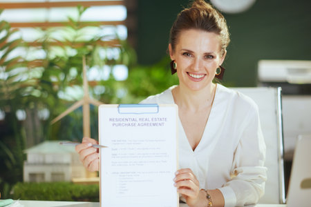 Sustainable real estate business. smiling elegant female realtor in modern green office in white blouse with clipboard and document.の写真素材