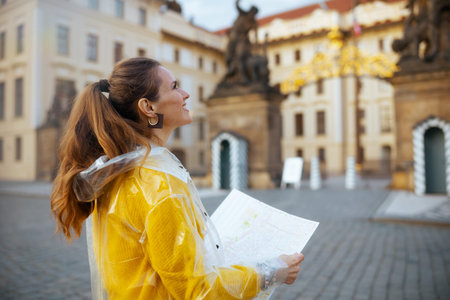 surprised young woman in yellow blouse and raincoat in Prague Czech Republic with map near Prague...