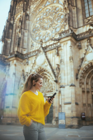 happy trendy middle aged traveler woman in yellow blouse in Prague Czech Republic having walking tour, using smartphone and walking.の写真素材