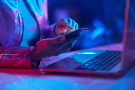 Neon metaverse futuristic concept. Closeup on woman with laptop using smartphone app in office.の写真素材