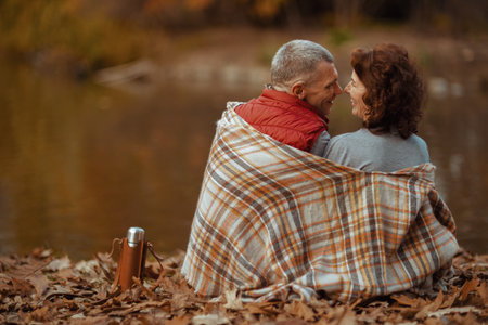 Hello autumn. Seen from behind modern couple in the park with blanket hugging.の写真素材