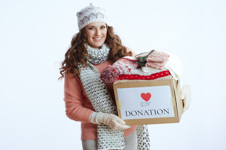Hello winter. smiling stylish middle aged woman in sweater, mittens, hat and scarf with donation box isolated on white.の写真素材