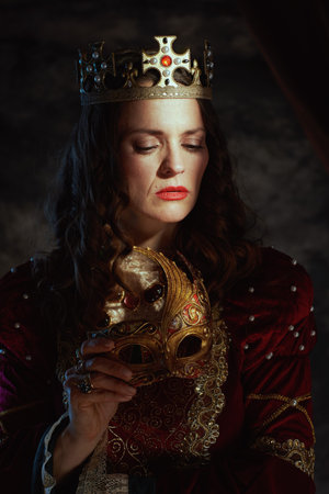 medieval queen in red dress with venetian mask and crown on dark gray background.の写真素材