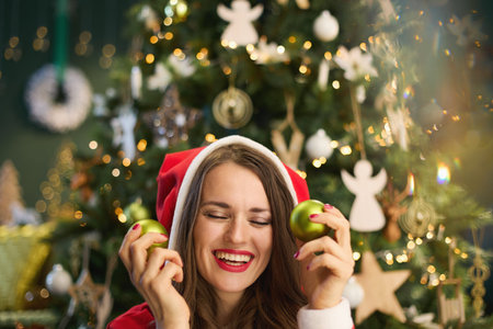 Christmas time. smiling modern housewife with Santa hat and Christmas ball near Christmas tree in the modern house.の写真素材