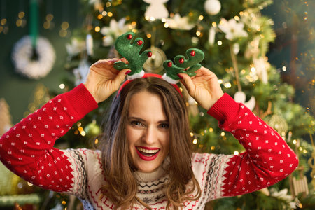 Christmas time. happy trendy woman with funny reindeer antlers headpiece hoop in traditional...