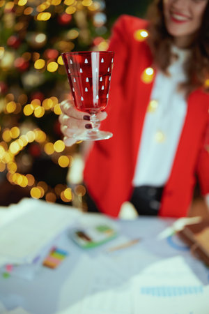 Christmas time. Closeup on smiling in red jacket with wineglass in santa hat in green office with Christmas tree.の写真素材