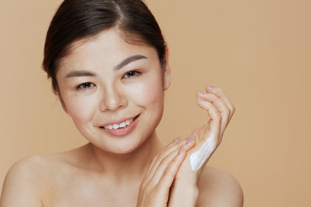 Portrait of young asian woman with hand cream on beige background.の写真素材