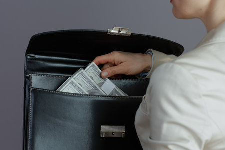 Closeup on small business owner woman in a light business suit with briefcase and dollars money packs isolated on gray.の写真素材