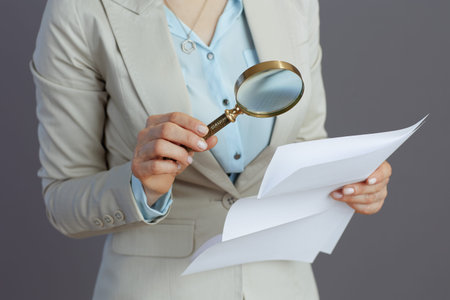 Closeup on small business owner woman in a light business suit with magnifying glass and document...