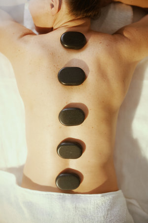 Healthcare time. Upper view of relaxed woman in massage cabinet having hot stone massage and laying on massage table.の写真素材