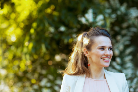 happy modern female in pink dress and white jacket in the city against greenery.の写真素材