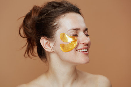 smiling modern 40 years old woman with eye patches isolated on beige background.の写真素材