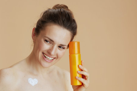 smiling modern middle aged woman with cosmetic cream jar and heart shaped cream on chest isolated on...
