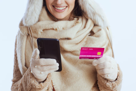 Closeup on happy woman against white background in white gloves with credit card using smartphone.の写真素材