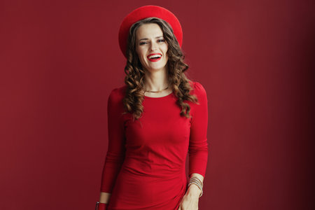 Happy Valentine. Portrait of happy stylish 40 years old woman with long wavy hair in red dress and beret on red background.の写真素材