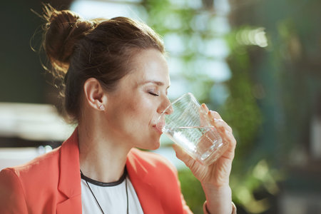 Sustainable workplace. modern business woman in modern green office in a red jacket with cup of...