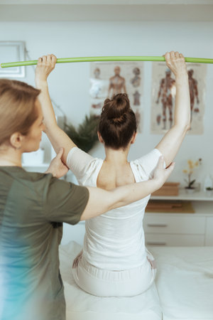 Healthcare time. Seen from behind female medical massage therapist in massage cabinet with client doing checkup.の写真素材