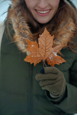 Closeup on smiling female outdoors in the city park in winter with mittens and autumn leaf.の写真素材