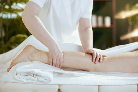 Healthcare time. Closeup on massage therapist in spa salon massaging clients leg on massage table.の写真素材