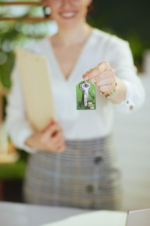 Time to move on. Closeup on young female realtor in modern green office in white blouse with clipboard and keys.の写真素材