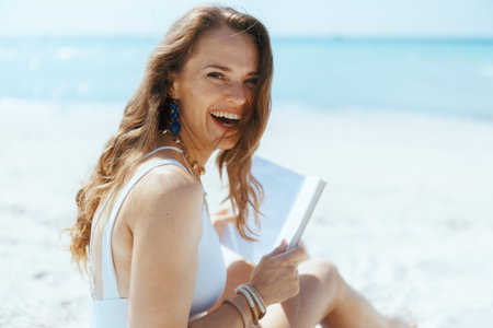 smiling stylish woman on the beach with straw bag and book.の写真素材