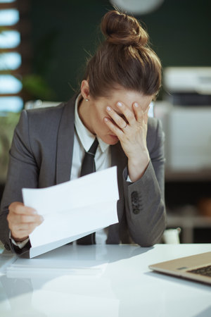 New job. sad modern middle aged woman worker in modern green office in gray business suit with employee termination letter.の写真素材