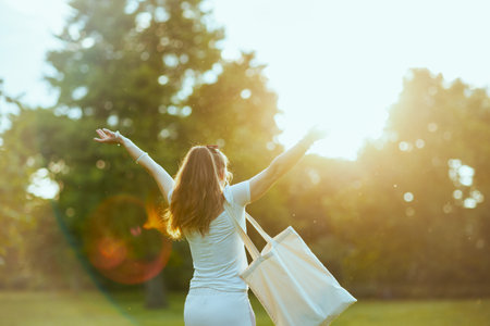 Summer time. smiling stylish female in white shirt with tote bag rejoicing in the meadow outdoors.の写真素材