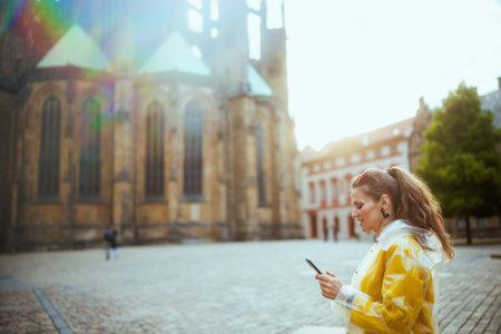 happy stylish traveler woman in yellow blouse and raincoat in Prague Czech Republic with smartphone having excursion.の写真素材