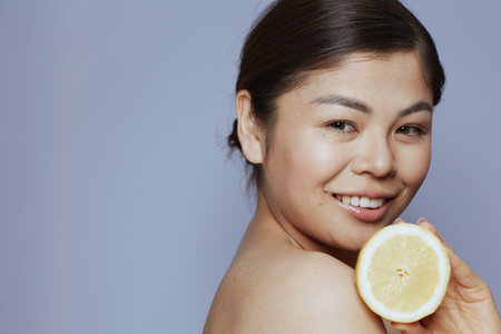 Portrait of young asian woman with lemon against blue background.の写真素材