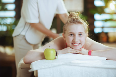 Healthcare time. female medical massage therapist in massage cabinet with teenage client and an apple making massage on massage table.の写真素材