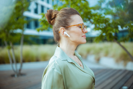 relaxed modern business woman near business center in green blouse and eyeglasses with wireless headphones.の写真素材