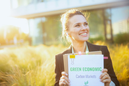 happy modern woman worker near business center in black jacket with documents, green economy plans, folder and wireless headphones.の写真素材