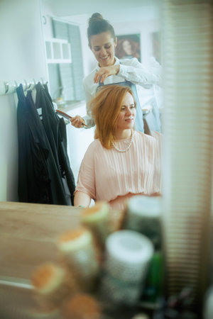middle aged woman hairdresser in modern hair studio with hairbrush and client.の写真素材