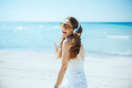 happy stylish woman on the seashore with headphones and smartphone dancing.の写真素材