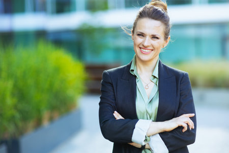 Portrait of happy modern woman worker near business center in black jacket with crossed arms.の写真素材