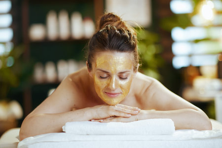 Healthcare time. relaxed modern 40 years old woman in spa salon with golden cosmetic mask on face laying on massage table.の写真素材