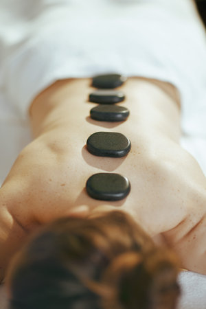 Healthcare time. Closeup on relaxed woman in massage cabinet having hot stone massage and laying on...