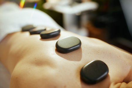 Healthcare time. Closeup on relaxed woman in massage cabinet having hot stone massage and laying on massage table.の写真素材