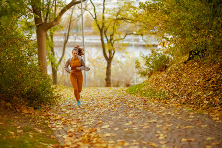 Hello autumn. Full length portrait of 40 years old woman in fitness clothes jogging in the park.の写真素材