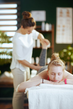 Healthcare time. massage therapist woman in massage cabinet with teenage client making massage on massage table.の写真素材